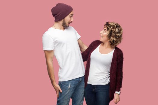 No way. Portrait of excited couple of friends in casual style standing and looking to each other with amazing faces, big eyes and toothy smile. Isolated, indoor, studio shot, pink background