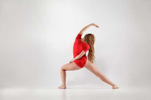 athletic blonde woman in red leotard doing yoga urdhva virabhadrasana pose . isolated indoor studio shot on light gray background. healthy lifestyle and leisure activity concept.