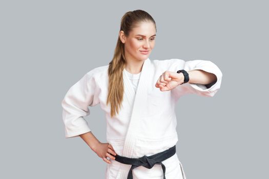 Burning calories. Athletic satisfied young blonde woman looking at smart watch counting burned calories during workout training, using fitness bracelet. Indoor studio shot, isolated on grey background