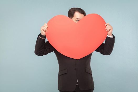 Love, st. valentine's concept. Businessman holding big heart, worry, panic. Indoor, studio shot, isolated on light blue or gray background