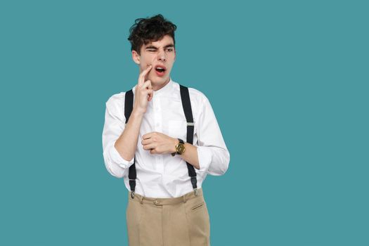 Tooth pain. man touching his chin because toothache. Portrait of handsome hipster curly young businessman in classic casual white shirt and suspender standing. studio shot isolated on blue background.