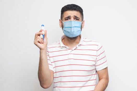 39 degress. Scared panic worry sick man with surgical medical mask standing, holding thermometer are shoched for high temperature, looking at camera. Indoor, isolated, white background, studio shot