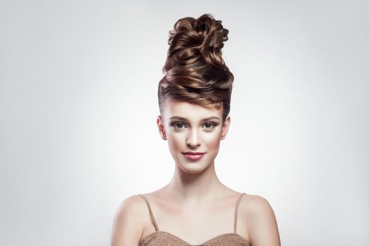 portrait of attractive brunette woman with stylish hairdo and makeup looking at camera with smimle on isolated grey background. indoor, studio shot on copy space.