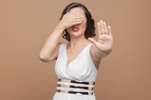 No, ban! middle aged woman don't need see this. Emotional expressing woman in white dress, red lips and dark curly hairstyle. Studio shot, indoor, isolated on beige or light brown background