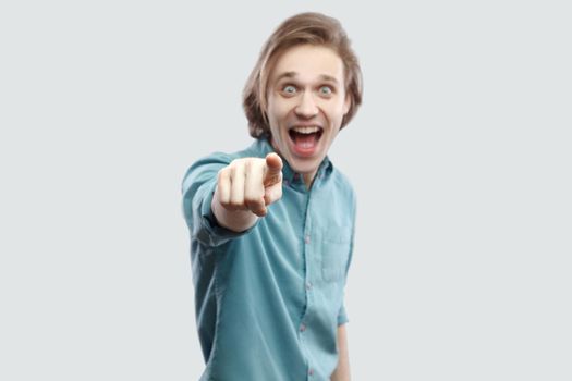 Wow. Portrait of amazed handsome long haired blonde young man in blue casual shirt standing, pointing, surprised and looking at camera. indoor studio shot, isolated on light grey background.
