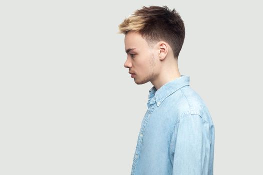 Profile side view portrait of calm serious handsome young man in light blue shirt standing and looking forward with serious face. indoor studio shot on grey background copy space.