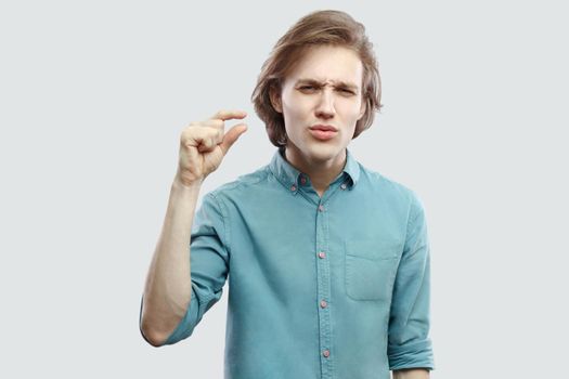 Please gime me a few more. Portrait of hopeful handsome long haired blonde young man in blue casual shirt standing and showing small gesture. indoor studio shot, isolated on light grey background.