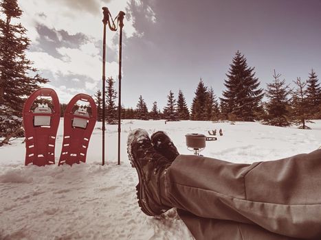 Red snowshoes and trekking poles ready in snow, winter vacation in mountains.  Winter mountain trail in snowy landscape. Nise sunny weather.