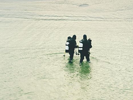 Prerow Germany - January 25 2018: Couple of sea divers walk from sea to beach. End of diving lesson.