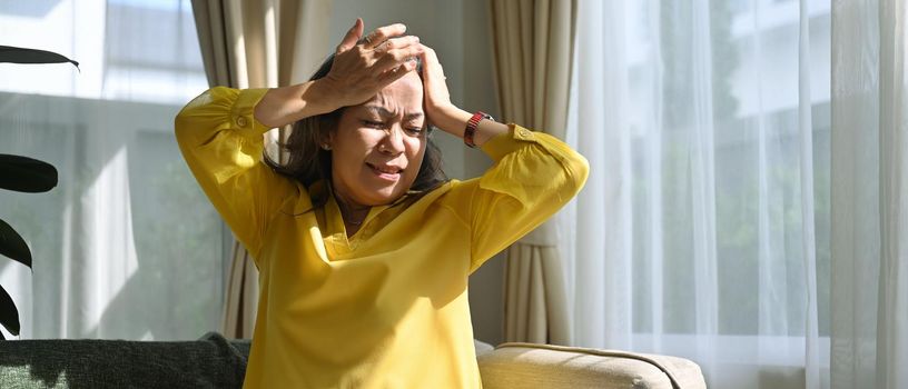 Unhealthy mature woman touching her head suffering from headache, migraine or dizziness. Age, medicine, health care and people concept.