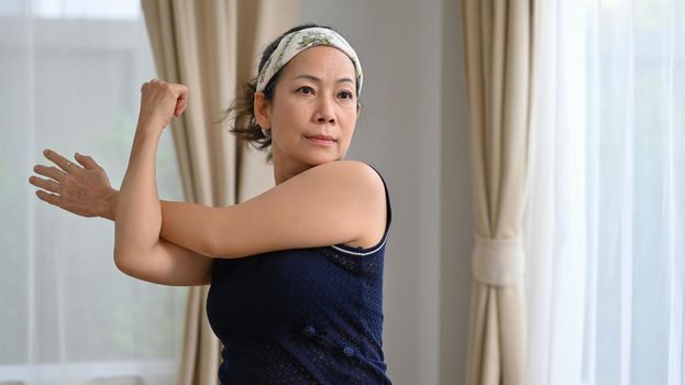 Active middle aged lady warming up, stretching her arms before workout at home. Healthy lifestyle and sport concept.