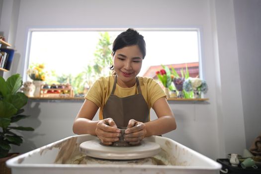 Smiling young asian woman making ceramic tableware on the pottery wheel in creative studio workshop.