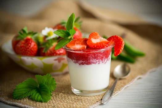 sweet homemade yogurt with strawberry jam and fresh strawberries in a glass cup, on a wooden table.