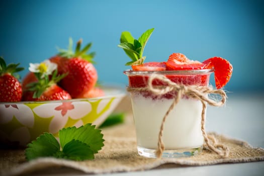 sweet homemade yogurt with strawberry jam and fresh strawberries in a glass cup, on a wooden table.