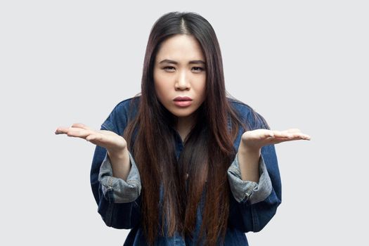Portrait of anger beautiful brunette asian young woman in casual blue denim jacket with makeup standing raised arms and asking. indoor studio shot, isolated on light grey background.
