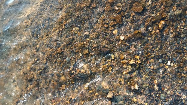 Top view on colorful pebbles covered by water. Close up view of smooth round pebble stones on the beach.