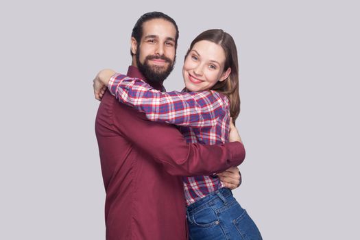 Portrait of happy satisfied bearded man and woman in casual style standing and hugging each other and looking at camera with toothy smile. indoor studio shot, isolated on gray background.