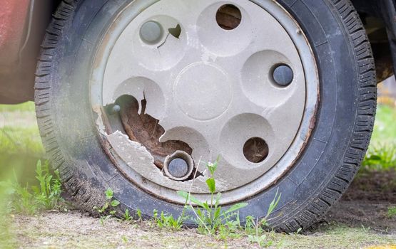 Weathered car wheel with dirt and grime. Rusty abandoned car in the parking lot. Restoration of a retro car. Flat tire. Vintage wheel with classic red car cap