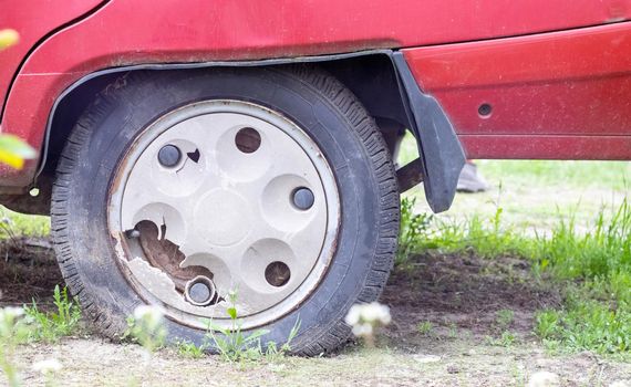 Weathered car wheel with dirt and grime. Rusty abandoned car in the parking lot. Restoration of a retro car. Flat tire. Vintage wheel with classic red car cap