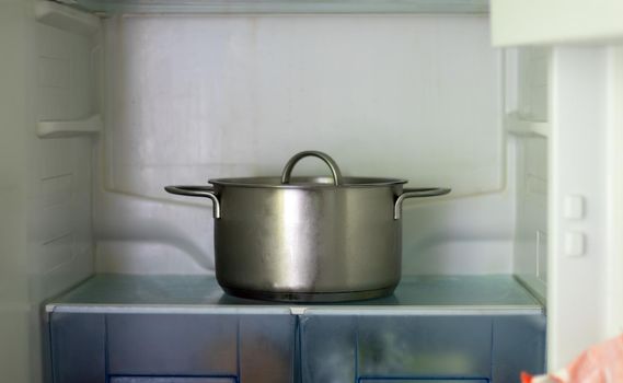 Freezer open pot close-up. Saucepan in an open refrigerator. The refrigerator inside is almost empty due to the economic crisis. Open refrigerator shelves with various cooked food