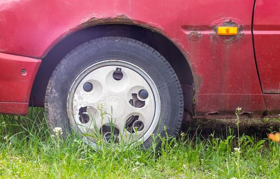 Weathered car wheel with dirt and grime. Rusty abandoned car in the parking lot. Restoration of a retro car. Flat tire. Vintage wheel with classic red car cap