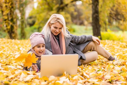 Beautiful young family lying on a picnic blanket, enjoying an autumn day in park while using laptop.