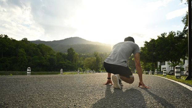Sports man in starting position, ready to run outdoors with beautiful sunset in background. Make effort for victory, sport and healthy lifestyle concept.