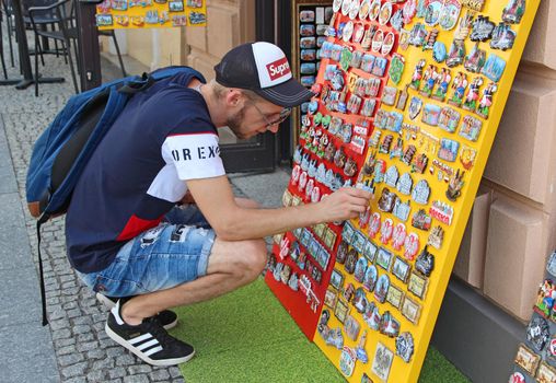 Modern guy buying souvenir at souvenir shop in Warsaw. Keepsake magnet for tourists. Young tourist chooses icon about Warsaw. Collection of magnets to sell to tourists