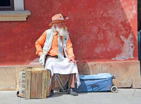 gray-haired old man sitting near accordion. Accordion stands next to old man with cigarette. Old musician earning his living by playing concertina. Old man street musician resting smoking cigarette