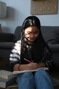 Little asian girl sitting in bright living room and doing homework.