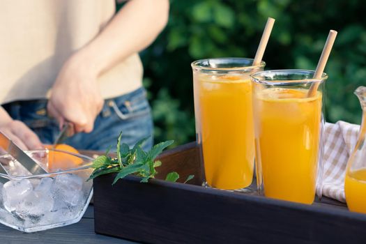 Girl cooking summer orange cocktail with mint and ice cubes outdoors, selective focus.