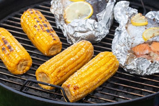 Several ears of corn are roasted on a round grill.