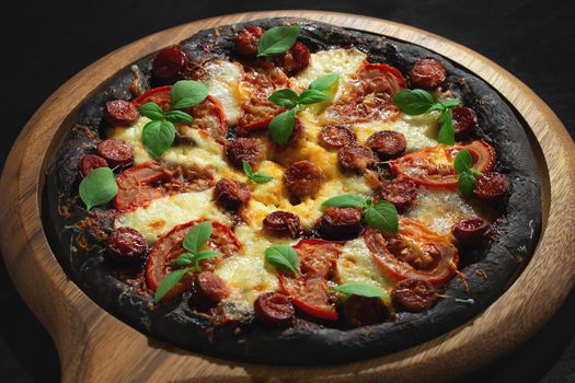 Black pizza with tomatoes, sausages, mozzarella and basil. Dough with healthy bamboo charcoal powder.