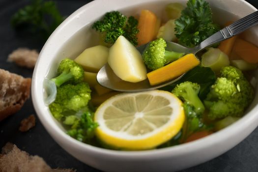 Vegetarian vegetable soup with carrots, broccoli and parsley in a light bowl on a metal tray on a wooden table.