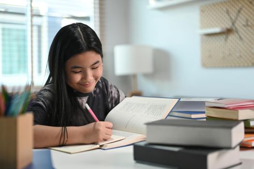 Smiling teenage girl doing homework at home.