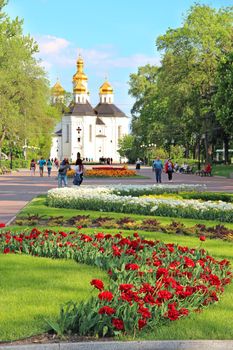 people have a rest in city park with beds of tulips in spring. Chernihiv town with blossoming tulips in spring. Beautiful Ukrainian town. Colors of spring. City decorations. People going in city park