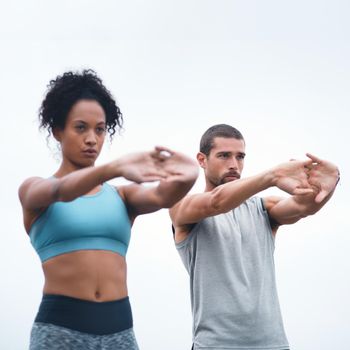 Shot of two sporty young people stretching while exercising outdoors.