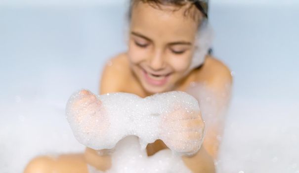 The child bathes in a bathtub soapy water. Selective focus.
