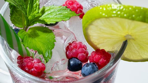 Refreshing summer cocktail with ice, lime and berries in a glass with a straw.