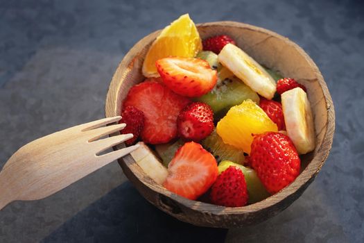 Fruit salad in a natural bowl made from half a coconut shell on a metal tray.