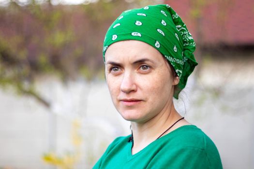 Portrait, close-up. Beautiful young woman without makeup in green t-shirt and green sun hat on a sunny summer day outdoors. Sunbeam. Caucasian woman gardener or farmer wears a modern headscarf