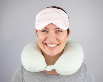 Smiling caucasian woman with travel pillow and sleeping mask isolated on white background