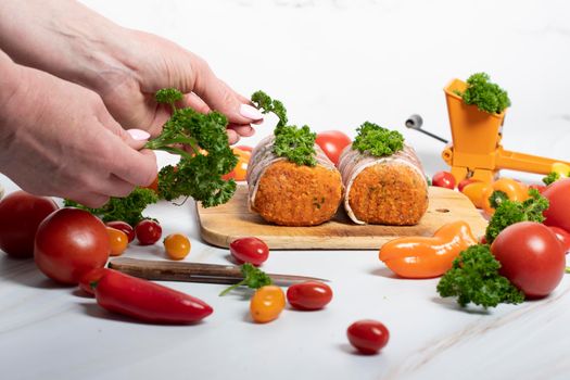 female hands sprinkle ground parsley on minced meat sausages in bacon with green parsley and fresh vegetables, cherry tomatoes, bell peppers, colorful food . High quality photo