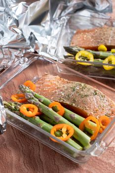 raw red salmon with salt and spices with green asparagus and paprika in a baking dish covered with foil. High quality photo