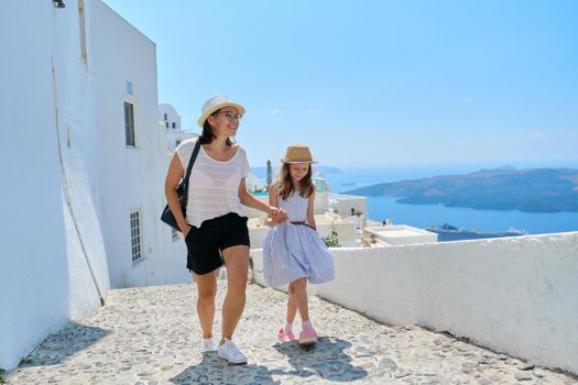 Happy tourists family mother and daughter kid walking on the Greek island of Santorini. Scenic marine and traditional architectural landscape background