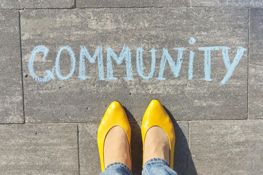 Community concept, top view on woman legs and text written in chalk on gray sidewalk.