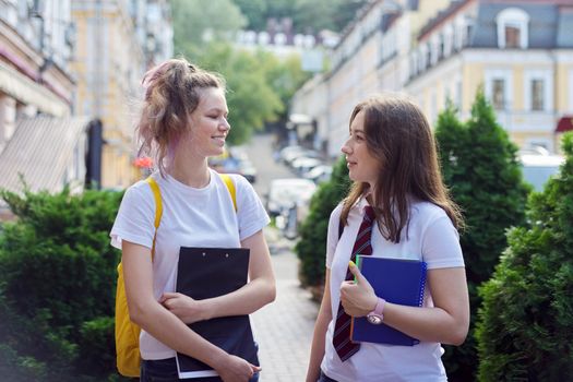 Two girl students talking on a city street, teenagers with backpacks, in white t-shirts
