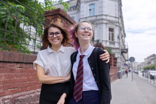 Mother and teenage daughter walking together on city street. Talking mom and girl student, parent and child discussing school, study