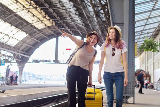 People walking with suitcase at the railway station. Happy mother and teenager daughter traveling with luggage together. Transport, tourism, moving, family concept