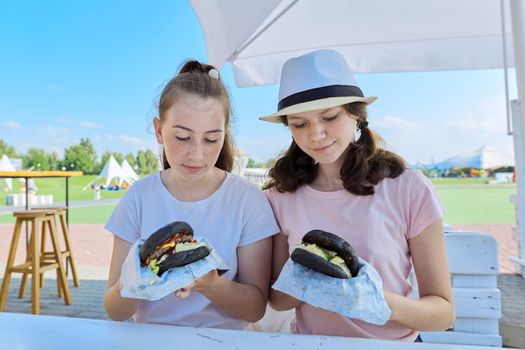 Teens two girls friends eating black burgers fast food, street food.